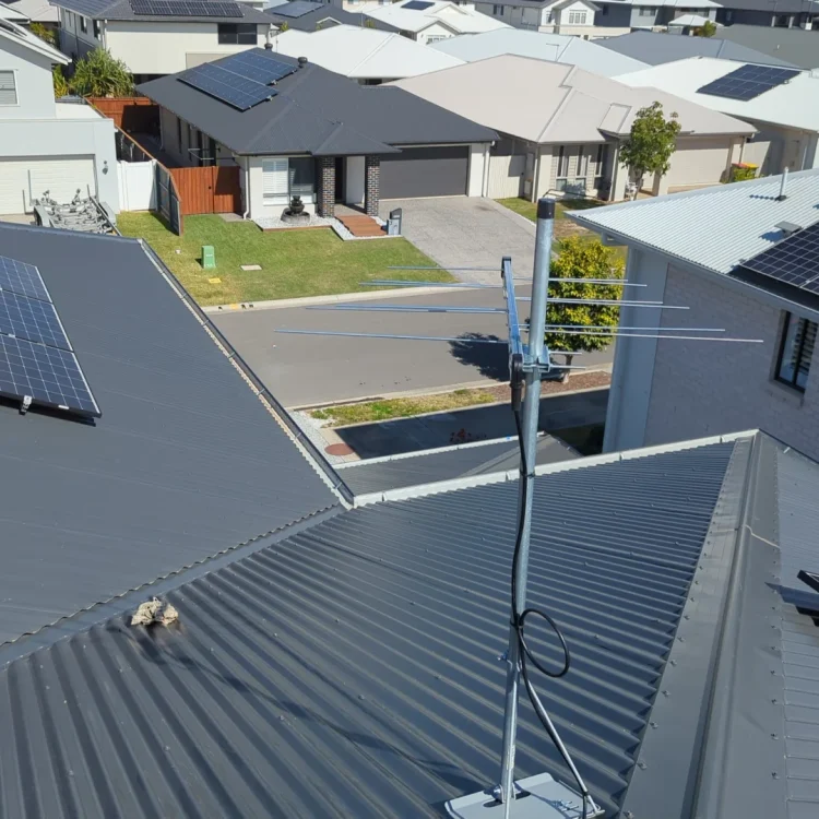 A tv antenna on a dark grey tin roof looking out at multiple houses around it